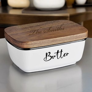 May include: White ceramic butter dish with a wooden lid. The lid has the text "The Smiths" engraved on it. The dish has the word "Butter" written in black cursive on the front.