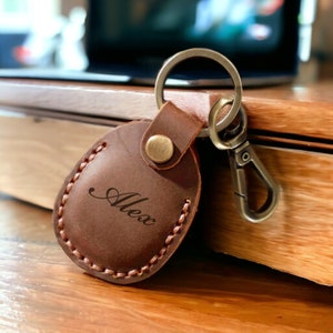 May include: Brown leather keychain with a metal ring and clasp. The leather is embossed with the name "Alex".