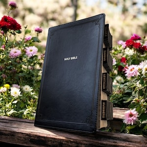 Peut inclure: Une Sainte Bible en cuir noir avec des lettres dor&eacute;es. Le livre est ouvert, r&eacute;v&eacute;lant des onglets &eacute;tiquet&eacute;s pour diff&eacute;rents livres de la Bible. L'arri&egrave;re-plan pr&eacute;sente des fleurs et de la verdure color&eacute;es, cr&eacute;ant un cadre serein.