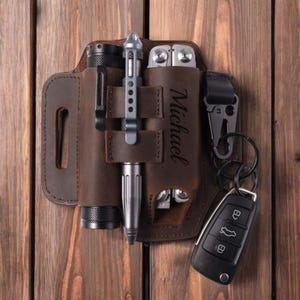 Puede incluir: Portaherramientas multiusos de cuero marrón con una linterna, un bolígrafo y una herramienta multiusos. El portaherramientas tiene un bucle para el cinturón y un llavero. El portaherramientas está personalizado con el nombre "Michael".