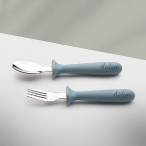 May include: A set of two blue baby utensils with stainless steel spoon and fork. The handles are personalized with the name "Aidan".