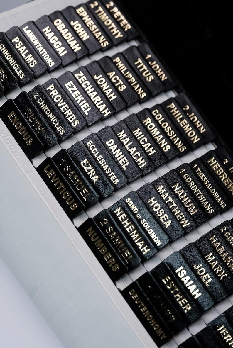 Peut inclure: Gros plan sur une Bible avec des onglets noirs portant des inscriptions dor&eacute;es. Les onglets sont &eacute;tiquet&eacute;s avec des noms de livres tels que &laquo;&nbsp;Exode&nbsp;&raquo;, &laquo;&nbsp;Psaumes&nbsp;&raquo; et &laquo;&nbsp;Proverbes&nbsp;&raquo;. Le livre est ouvert, r&eacute;v&eacute;lant les onglets.