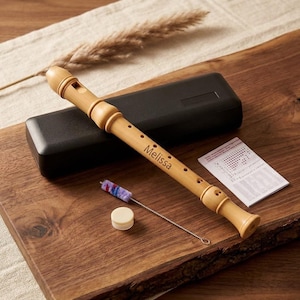 May include: A light brown wooden recorder instrument featuring the name Melissa engraved on the body. The set includes a black rectangular carrying case, a small white circular cap, a thin metal cleaning brush with purple bristles, and a fingering chart.