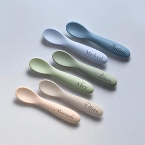 May include: Six personalised silicone baby spoons in various colours, including blue, green, and beige. Each spoon has a name engraved on the handle: Aidan, Michael, Liam, Alex, Olivia, and Amanda.
