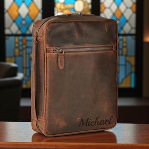 May include: A brown leather briefcase with a zipper closure and a front pocket. The briefcase has a handle on the side and the name "Michael" is engraved on the front. The leather has a distressed look.
