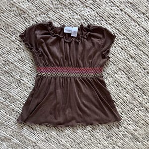 May include: A brown short-sleeved top with a decorative, patterned band at the waist. The top has a ruffled neckline and sleeves. The waist band has a red, pink, and gold pattern. The top is made of a soft material.