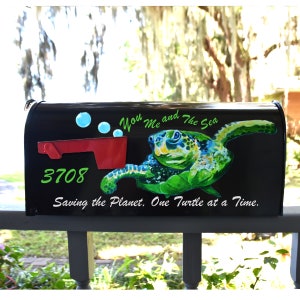 May include: A black mailbox with a green sea turtle painted on it. The turtle is swimming with bubbles around it. The mailbox has the text "You Me and The Sea" and "Saving the Planet. One Turtle at a Time." on it.