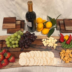 May include: A wooden serving tray with a black handle, filled with various snacks, including grapes, strawberries, crackers, cheese, and lemons. The tray is surrounded by four smaller wooden coasters.