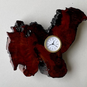 May include: A wooden clock with a dark brown finish, shaped like a heart, with a white clock face and gold hands. The clock is mounted on a wall.