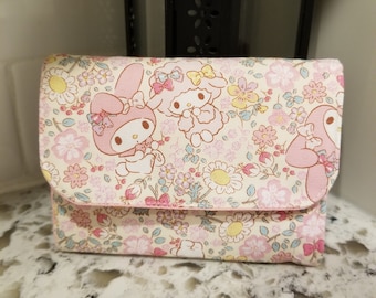 Puede incluir: Una cartera de tela rosa y blanca con un patrón floral y dos personajes de dibujos animados. Los personajes son un conejo rosa y un cordero blanco.
