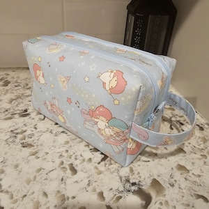 May include: Light blue zippered makeup bag with a Little Twin Stars design. The bag has a handle and features a white background with stars, musical notes, and the characters Little Twin Stars. The text "Little Stars" is printed on the bag.