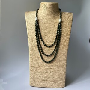 May include: A multi-strand necklace made of dark green beads with two white oval beads at the ends.