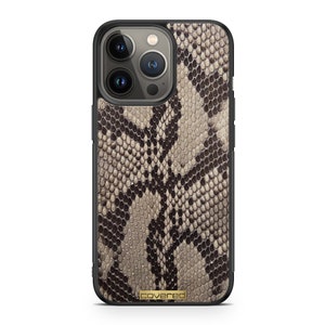 Peut inclure: Une coque de téléphone noire avec un motif en peau de serpent. La coque a un logo "covered" en or sur le bas.