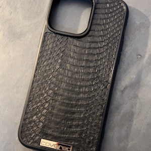 May include: Black phone case with a textured, snake-skin pattern and a gold "covered" logo.
