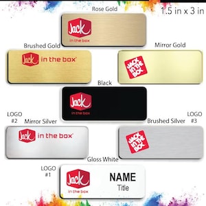 May include: A collection of Jack in the Box name badges in various finishes, including rose gold, brushed gold, mirror gold, black, mirror silver, brushed silver, and gloss white. Each badge features the Jack in the Box logo and the text "Jack in the box". The badges are 1.5 inches by 3 inches.