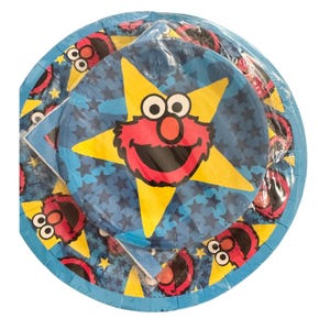 May include: A stack of round paper plates wrapped in clear plastic. The plates feature a dark blue background with a pattern of small stars, a large yellow star in the center, and a graphic of the red Elmo character from Sesame Street.