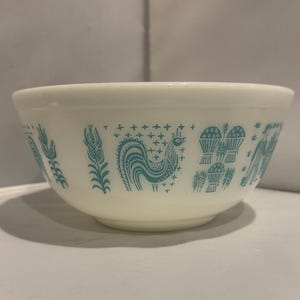 以下が含まれることがあります： オフホワイトのミキシングボウル。ターコイズブルーの雄鶏と農場のデザイン。ボウルは丸みを帯びた形で、厚く不透明な素材で作られています。デザインにはトウモロコシの穂、小麦、農夫が含まれています。