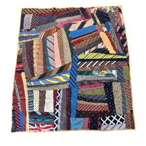 May include: A rectangular quilt constructed from a patchwork of various neckties in diverse colors, patterns, and textures. The design features a mix of stripes, polka dots, geometric shapes, and a Union Jack print, all stitched together with a gold border.