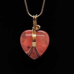 Pode incluir: Um colar de corrente de ouro com um pingente de cora&ccedil;&atilde;o rosa envolto em fio de ouro.