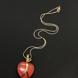 Pode incluir: Um colar de corrente de ouro com um pingente de cora&ccedil;&atilde;o rosa envolto em fio dourado.
