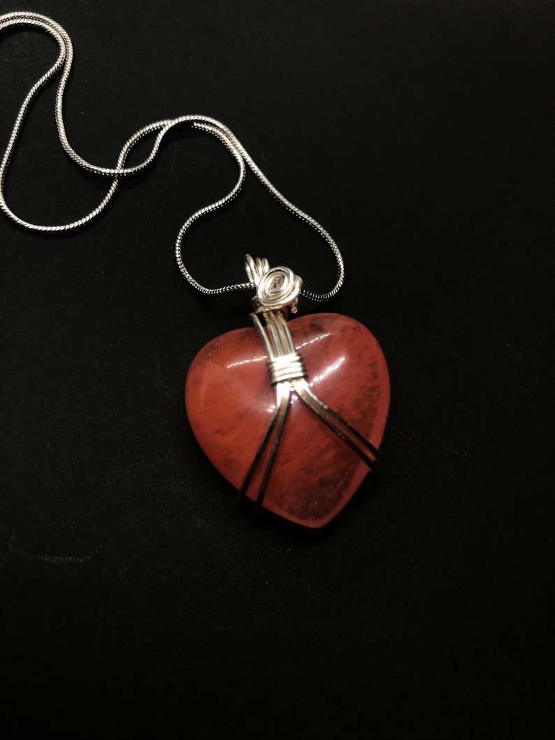 Pode incluir: Um colar de corrente de prata com um pingente de cora&ccedil;&atilde;o rosa envolto em fio de prata.