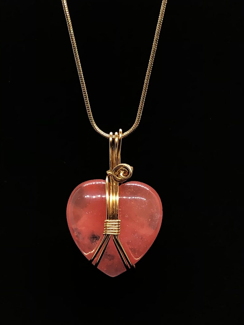 Pode incluir: Um colar de corrente de ouro com um pingente de cora&ccedil;&atilde;o rosa envolto em fio de ouro.
