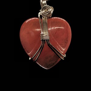 Pode incluir: Um pingente em forma de cora&ccedil;&atilde;o envolto em fio de prata com uma pedra de quartzo rosa rosa.