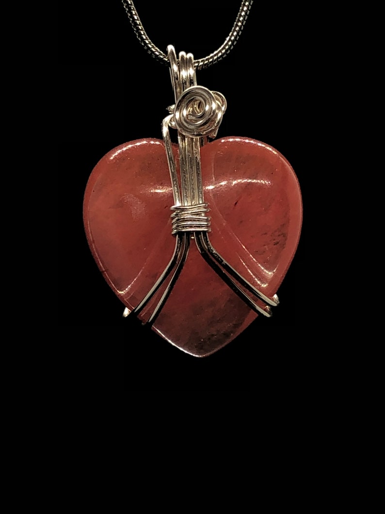 Pode incluir: Um pingente em forma de cora&ccedil;&atilde;o envolto em fio de prata com uma pedra de quartzo rosa rosa.