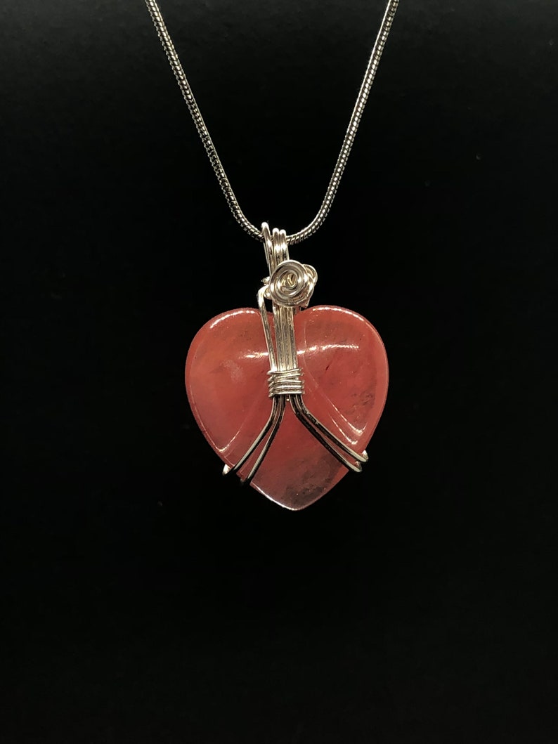 Pode incluir: Um colar de corrente de prata com um pingente de cora&ccedil;&atilde;o rosa envolto em fio de prata.