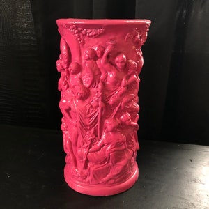 May include: A pink ceramic umbrella stand with a detailed relief design of figures in a classical style.