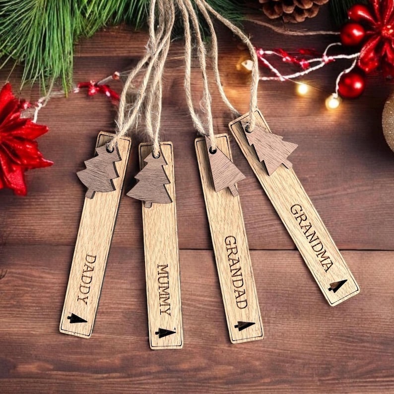May include: Five wooden Christmas tree ornaments with twine hangers. Each ornament has a small tree design and a name engraved on it: Daddy, Mummy, Grandad, Grandma.