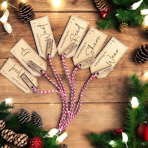 Peut inclure: Six étiquettes cadeaux en bois avec une ficelle attachée. Chaque étiquette porte une phrase différente, notamment "quelque chose que vous voulez", "quelque chose à lire", "quelque chose à partager" et "quelque chose à porter".