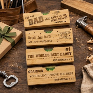 May include: Four wooden levels with engraved text, including "FOR THE DAD", "Great JOB DAD", "#1 THE WORLDS BEST DADDY", and "GRANDAD". Each level has a bubble vial and personalized messages. The levels are on a wooden surface.