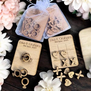 Puede incluir: Conjunto de juegos de boda de madera con tres juegos diferentes: un juego de lanzamiento de anillos, un juego de tres en raya y un juego con corazones y cruces. Los juegos est&aacute;n personalizados con los nombres "Lisa & Graham" y la fecha "31 de junio de 2025".