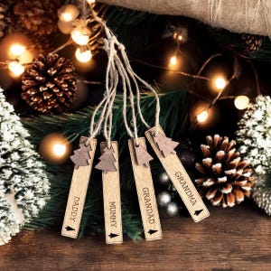 May include: Five wooden Christmas tree ornaments with twine hangers. Each ornament is engraved with a different name: "Daddy", "Mummy", "Grandad", "Grandma", and "Grandad".