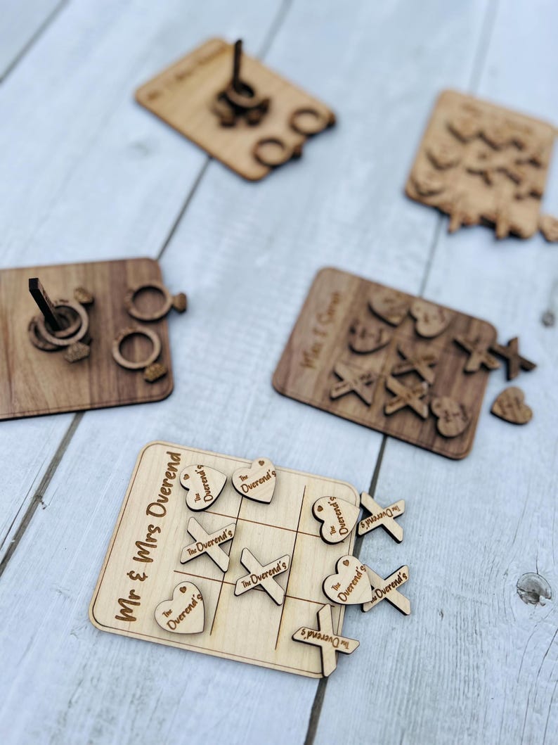 May include: A wooden game set with a tic-tac-toe board and pieces that say "The Overend's". The game is set up on a light wood surface. There are also other wooden pieces in the image, including a ring toss game and a wooden sign that says "Mr. & Mrs. Overend".