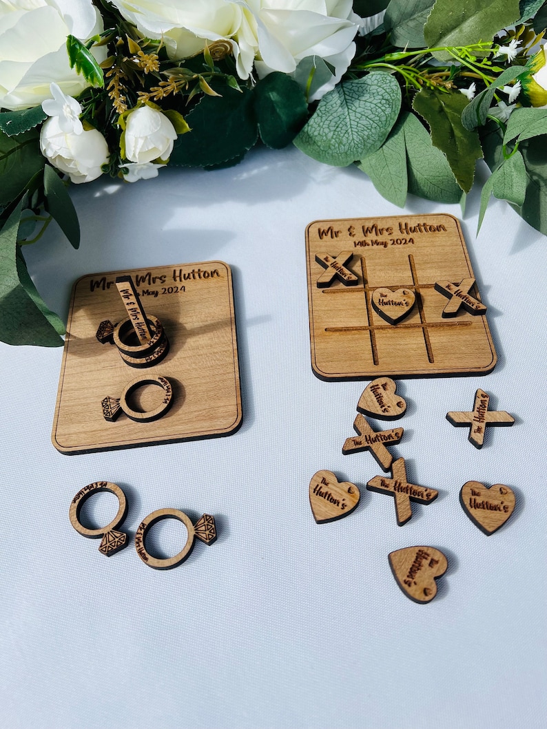 May include: A wooden wedding game with two boards. One board has a ring toss game with the text "Mr & Mrs Hutton 14th May 2024". The other board is a tic-tac-toe game with the text "Mr & Mrs Hutton 14th May 2024". There are also wooden hearts and X's that can be used to play the tic-tac-toe game.