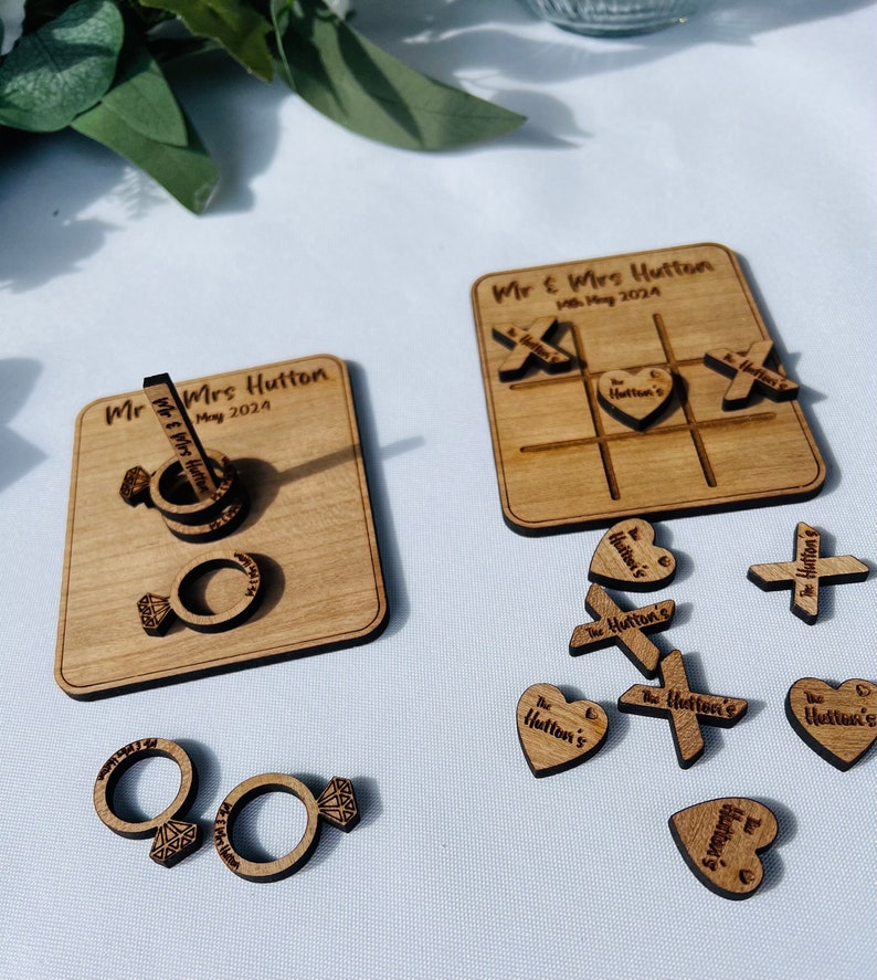 May include: Wooden wedding game set with a tic-tac-toe board and ring holder. The tic-tac-toe board has the text "Mr & Mrs Hutton" and "May 2024". The ring holder has the text "Mr & Mrs Hutton" and "May 2024".