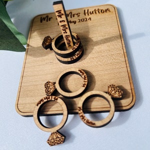 May include: Wooden ring toss game with four rings and a center post. The rings are engraved with "Mr. & Mrs. Hutton" and the date "May 2024".