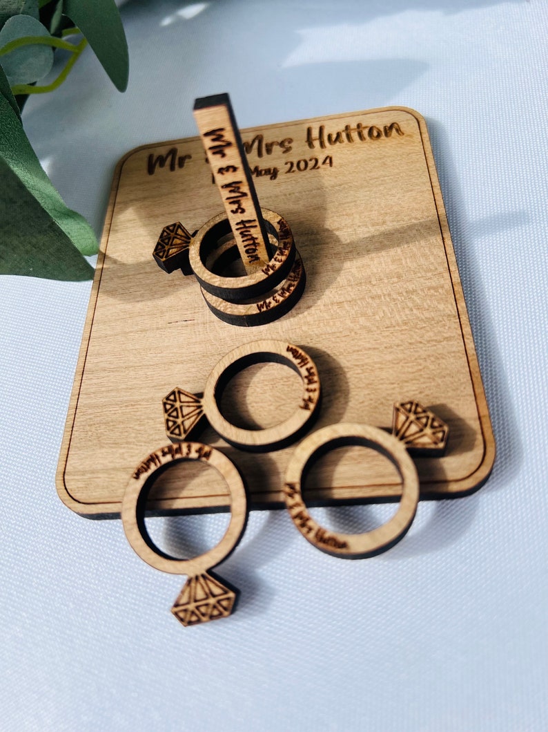 May include: Wooden ring toss game with four rings and a center post. The rings are engraved with "Mr. & Mrs. Hutton" and the date "May 2024".