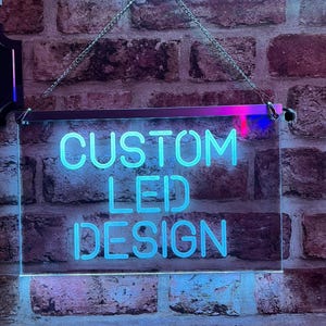 May include: A rectangular LED sign displaying "CUSTOM LED DESIGN" in bright blue neon. The sign is suspended by a chain and set against a brick wall. The sign's dimensions are not specified.
