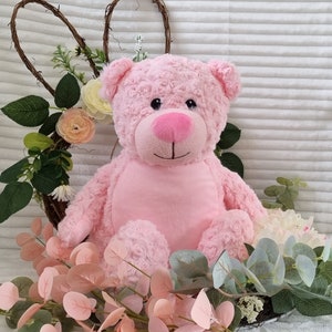 May include: A pink plush teddy bear with a pink nose and black eyes. The bear is sitting on a bed of pink and green leaves.