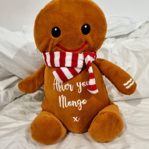 May include: A gingerbread man plush toy wearing a red and white striped scarf. The plush toy has a smiling face and the words "After you Mongo x" embroidered on its chest.