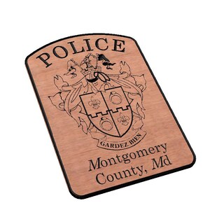 May include: A wooden plaque with a black border and the words "POLICE" in large letters. The plaque features a coat of arms with a shield, a crown, and the words "GARDEZ BIEN". Below the coat of arms is the text "Montgomery County, Md".