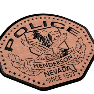May include: A brown wooden police badge with a black border and a black eagle design. The badge has the words "Police" in a black circle, "Henderson Nevada" on a banner, and "Since 1953" at the bottom.