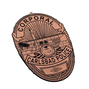 May include: A brown wooden badge with the text "Corporal Carlsbad Police" and a depiction of a building with a flagpole and a seal.