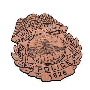 May include: A wooden badge with a brown background and black lettering. The badge features a stylised eagle with wings spread, a banner with the text "U.S. CAPITOL", a star, a depiction of the U.S. Capitol building, and the text "POLICE 1828".
