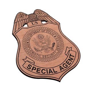 May include: A wooden badge with the text "US Department of State Diplomatic Security Services Special Agent" and an eagle design.