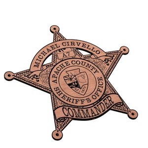 May include: A wooden sheriff's star badge with the text "MICHAEL CIRVELLO" and "APACHE COUNTY SHERIFF'S OFFICE" around the star. The badge also has the text "COMMANDER" on a ribbon.