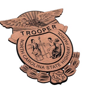 May include: A wooden badge with the words "North Carolina State Highway Patrol" and "Trooper" around a circle with an eagle and two figures inside. The badge has a brown wood grain finish and black lettering.